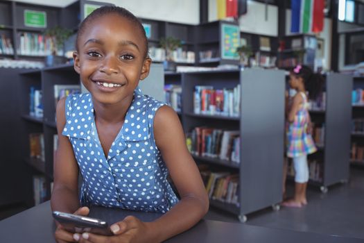 Smiling girl with mobile phone at desk in library