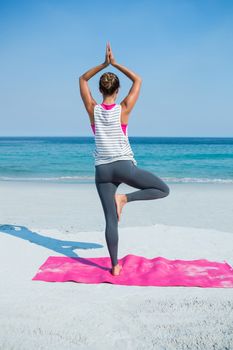 Rear view of woman practicing yoga in tree pose at beach on sunny day