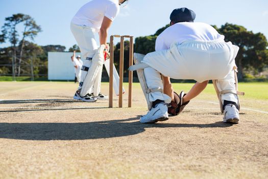 Rear view of wicket keeper crouching by stumps during match