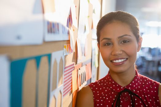 Smiling female executive standing near bulletin board in office