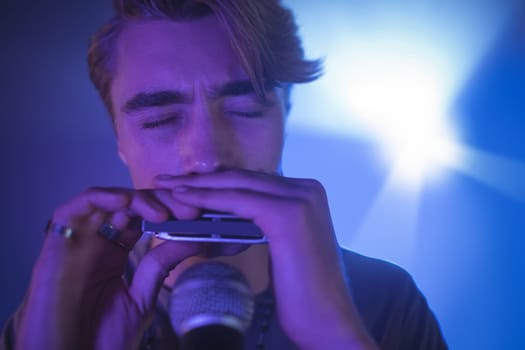 Male musician playing mouth organ in illuminated nightclub