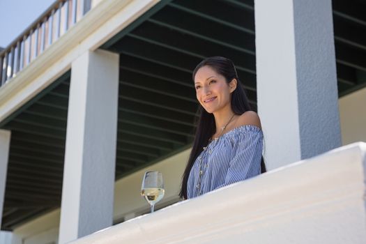 Smiling young woman standing by wineglass in balcony