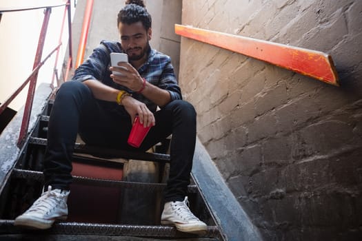 Man using mobile phone while having drink on staircase of bar