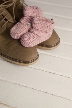 Baby booties with mans shoes on floor