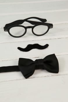 Bow tie, spectacles and fake moustache arranged on wooden plank