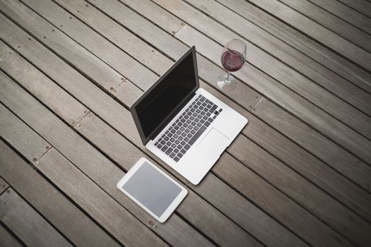 Laptop with digital tablet and wineglass on hardwood floor