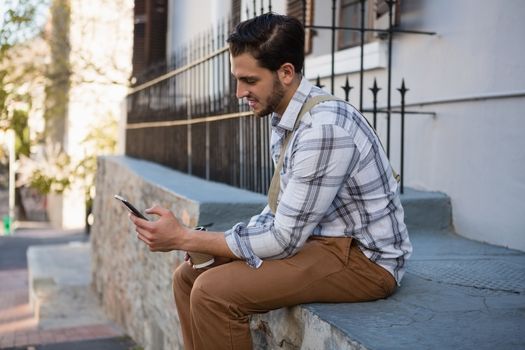  Man using mobile phone while sitting on retaining wall