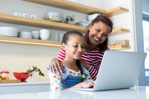 Mother and daughter using laptop in kitchen worktop