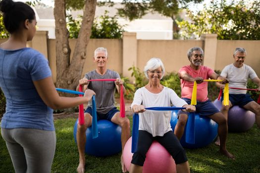 Trainer guiding senior people while exercising with ribbons and balls