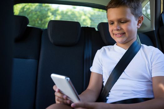 Teenage boy using mobile phone in the back seat of car