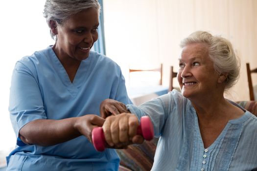 Nurse helping senior woman in lifting dumbell