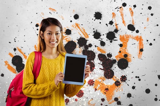 Happy young student woman holding a tablet against grey, yellow and black splattered background
