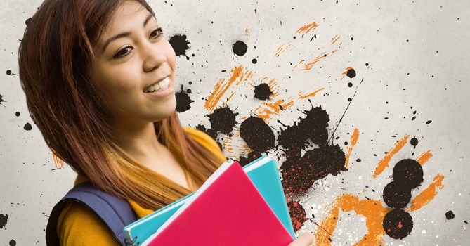 Happy young student woman holding notebooks against grey, yellow and black splattered background