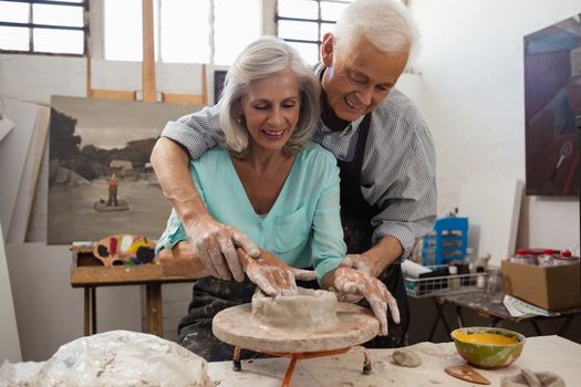 Senior man assisting senior woman in making pottery during drawing class