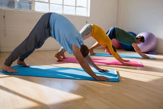 instructor with students practicing downward facing dog pose in yoga studio