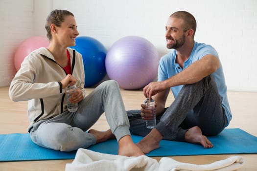 Instructor and female student talking while having water in yoga studio