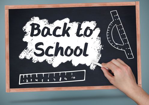 Hand writing back to school on blackboard with chalk and rulers