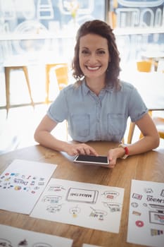 Smiling young woman sitting with digital tablet and papers at coffee shop