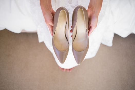 Low section of bride holding shoes while sitting in fitting room