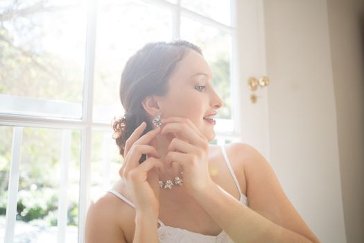 Beautiful bride wearing earring while standing by window