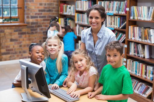 Cute pupils and teacher looking at computer in library