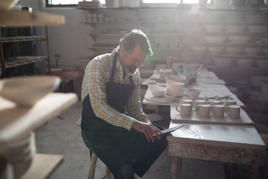 Male potter using digital tablet at worktop