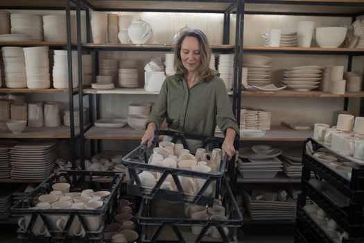 Female potter holding cups in crate
