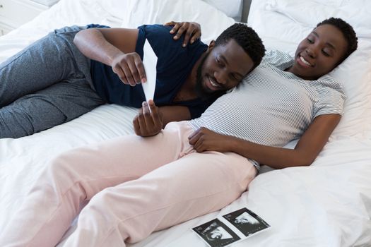 Man and pregnant woman looking at sonography in bedroom
