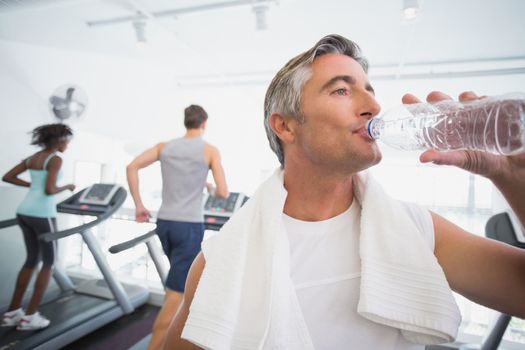 Fit man drinking water beside treadmills