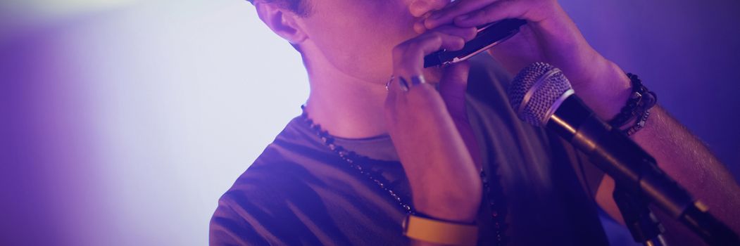 Confident man playing mouth organ in illuminated nightclub