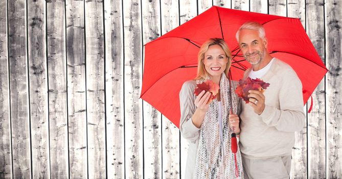 Autumn couple under umbrella in front of wood holding leaves