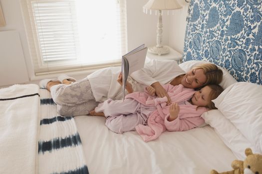 Mother with her daughter reading storybook in bedroom