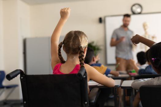 Rear view of disable schoolgirl raising hand in classroom