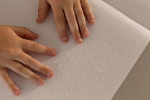 Blind boy hands reading a braille book in classroom