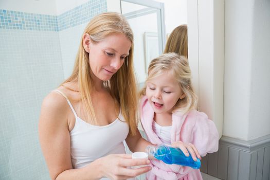 Happy woman pouring blue mouthwash with daughter