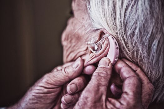 Doctor inserting hearing aid in senior patient ear