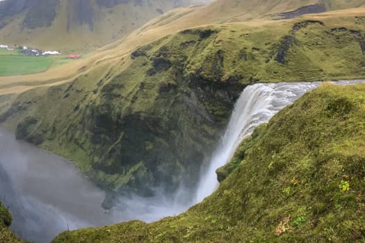 Skogafoss waterfall in Iceland top of waterfall during heavy rainfall between green rocks