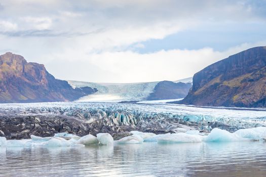 Vatnajoekull glacier in Iceland blue and ash colored ice melting into glacier lake