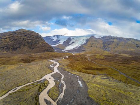 Vatnajoekull glacier in Iceland melting water from glacier forming river and cutting through grass land