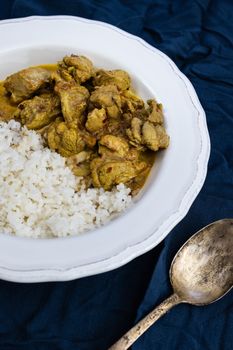 Orange spicy chicken curry and white basmati rice in a white plate on a dark blue background. Indian traditional cuisine.