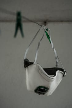 A white medical mask with green air filter hanging on a clothesline.