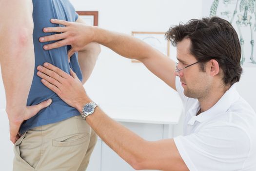 Side view of a male physiotherapist examining mans back
