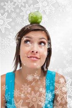 Composite image of attractive young woman standing upright with a green apple on her head