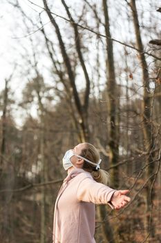 Portrait of caucasian sporty woman wearing medical protection face mask while relaxing by taking a deep breath in forest. Corona virus, or Covid-19, is spreading all over the world
