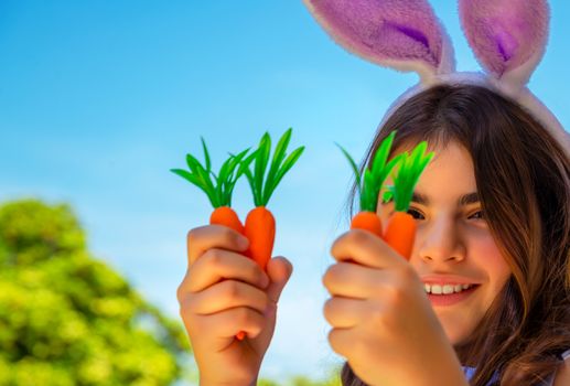 Portrait of a cute little bunny girl with carrots enjoying Easter, having fun gardening in the yard on a sunny day, traditional food for Easter celebration, happy spring holiday

