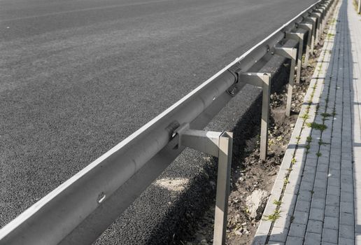 Close-up on a layer of new asphalt at the road under construction with a sidewalk road and bumper.