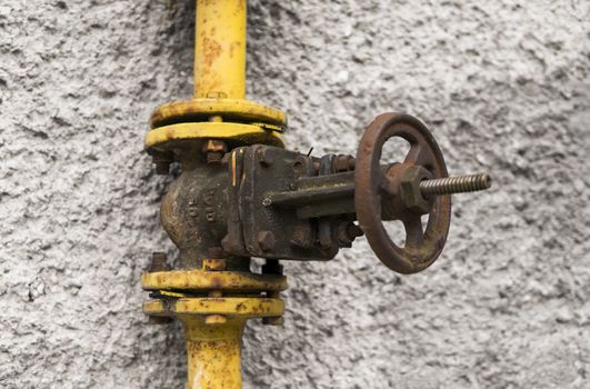 Old weathered gas crane and pipe on the background of a gray wall. Old gas gate of yellow colour is on a pipe and blocks a pipe. The pipeline with cranes for gas giving on the wall.