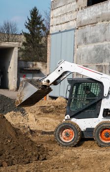 White skid steer loader at a construction site working with a soil. Industrial machinery. Industry.