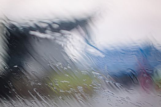 Rain Drops On Surface of wet Window Glass pane In Rainy Season. Abstract background. Natural Pattern of raindrops isolated from blurry city outdoor in a cloudy environment.