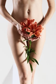 Intimate part of a woman's body with flower in hands. Close up of a woman body with flower on her pubes. No retouch.
